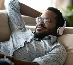 Image of a man lying on a couch with headphones, listening to music