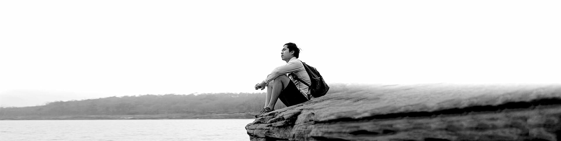 Image of a man sitting outside with a backpack, staring off into the distance