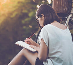 Image of a woman outdoors, writing in a journal